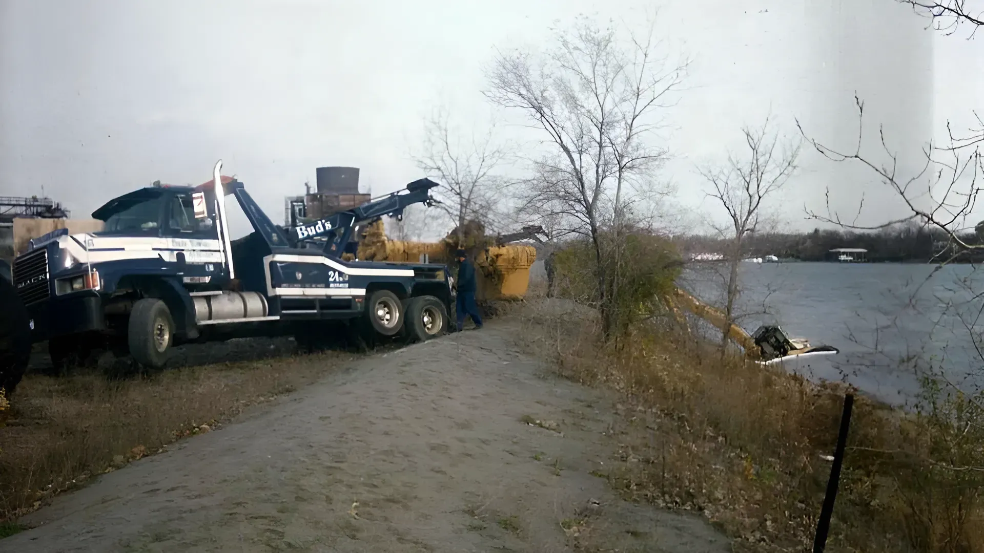 Tow truck near a body of water, attempting to pull a vehicle from the water. Cloudy day.
