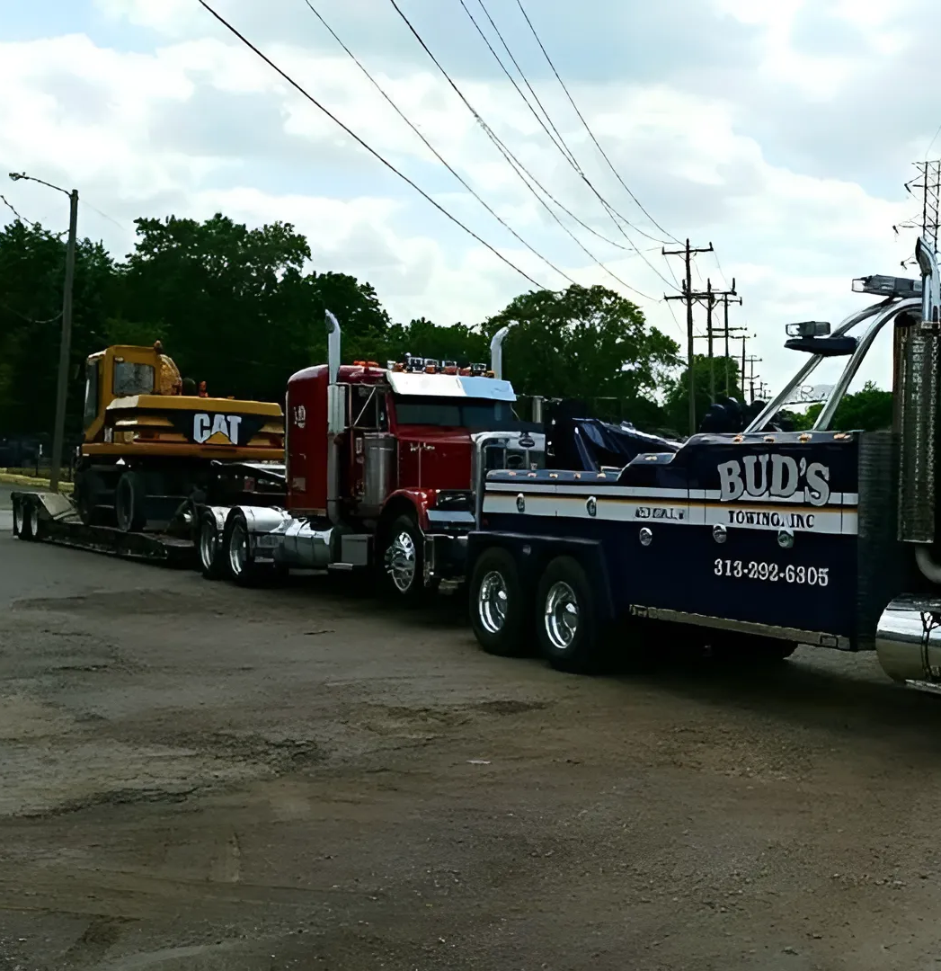 A large red semi-truck towing a Caterpillar excavator on a flatbed trailer, under cloudy skies.