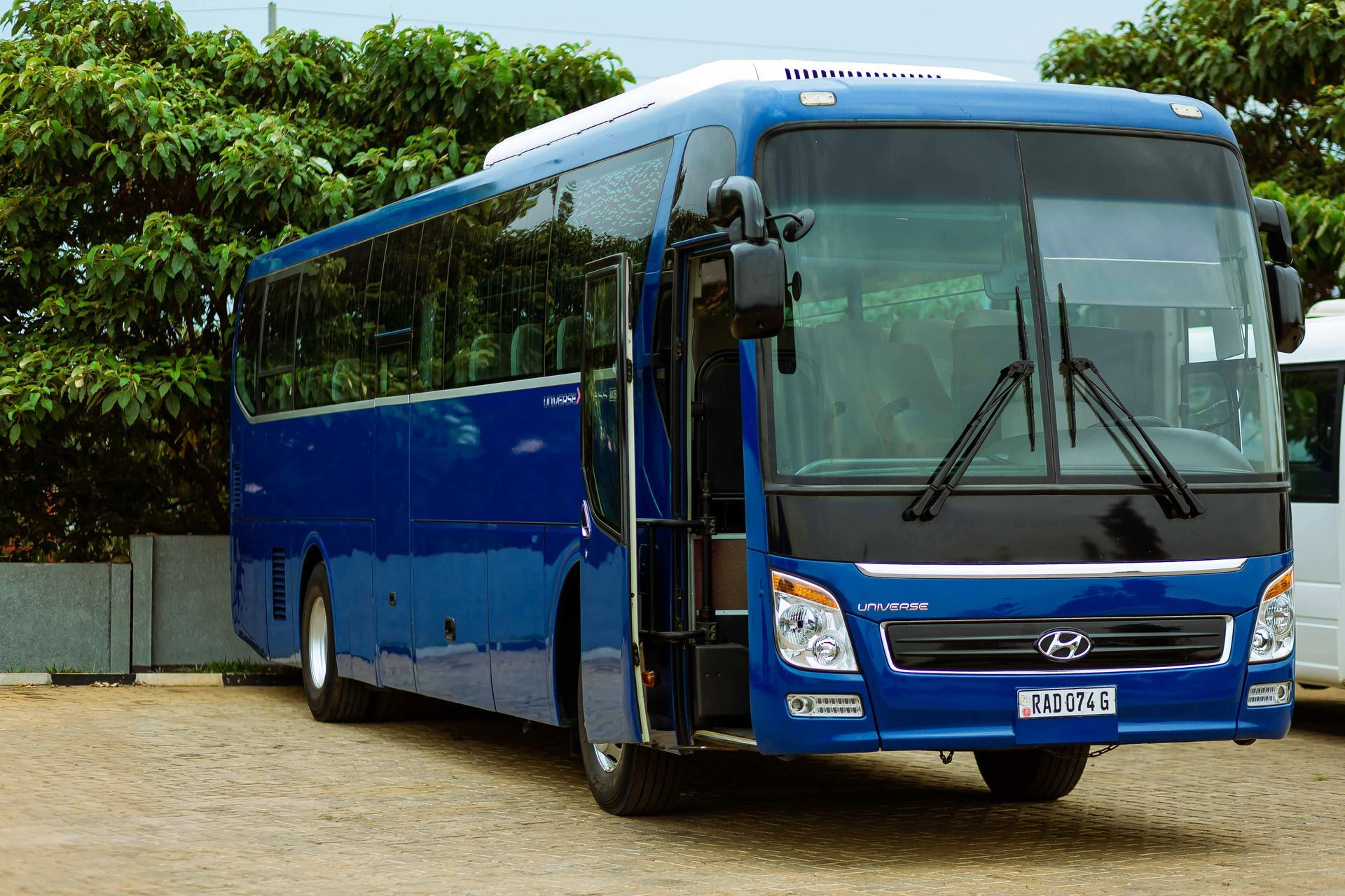 Blue Hyundai coach bus with open door, parked outdoors near trees.
