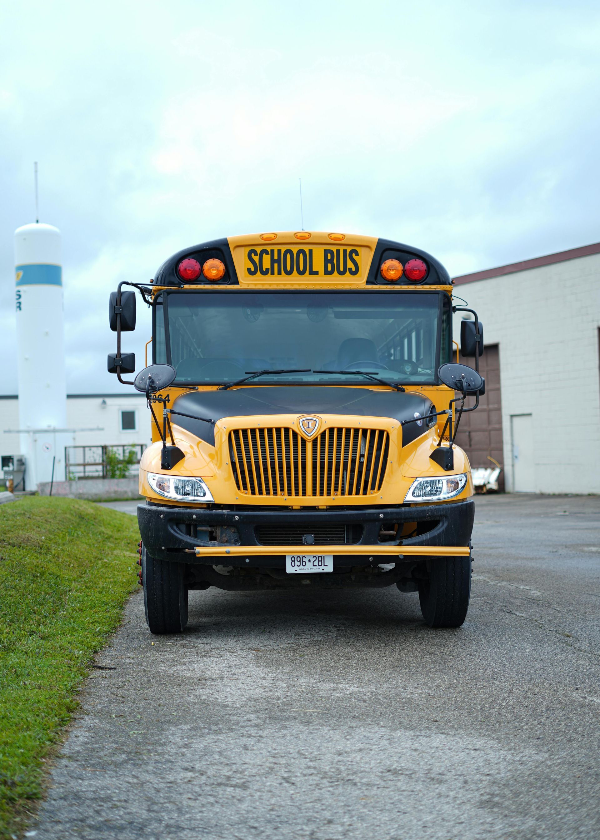 Yellow school bus parked on a gray path in front of a building; cloudy sky.