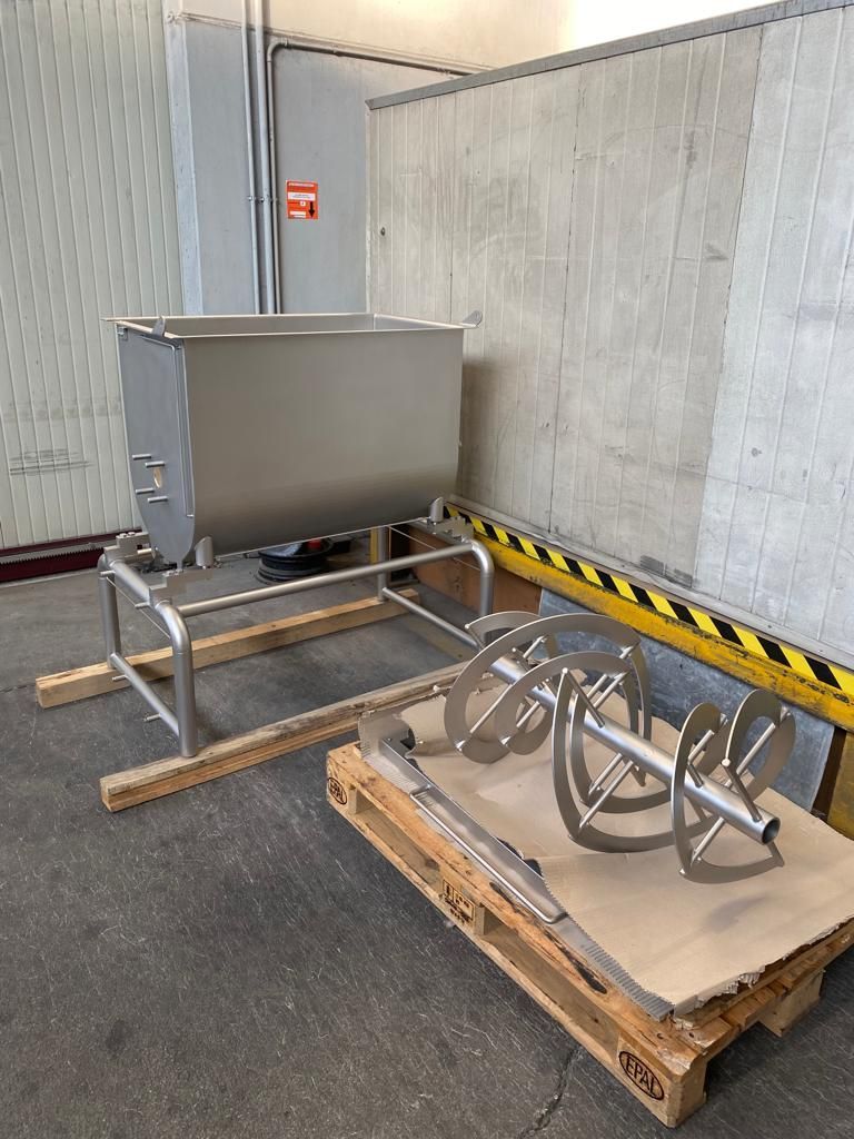 Un miscelatore in acciaio inossidabile è appoggiato su un pallet di legno in un magazzino.