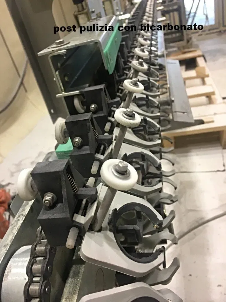 Macchinario industriale con file di rulli metallici e componenti neri in un ambiente di officina.