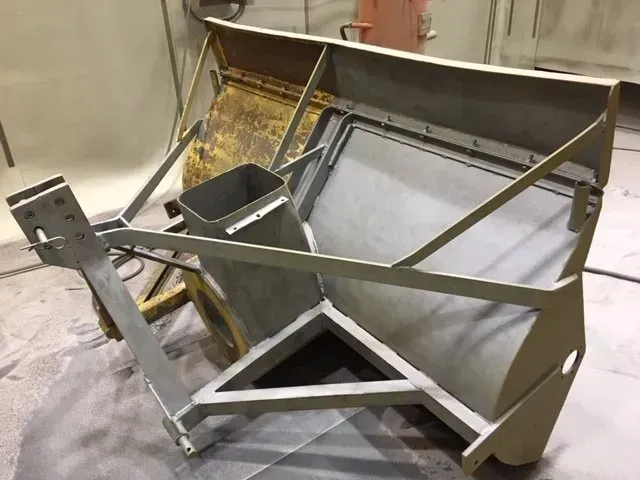 Telaio di carrello in metallo con supporti angolari e pannello a rete in un'officina industriale.