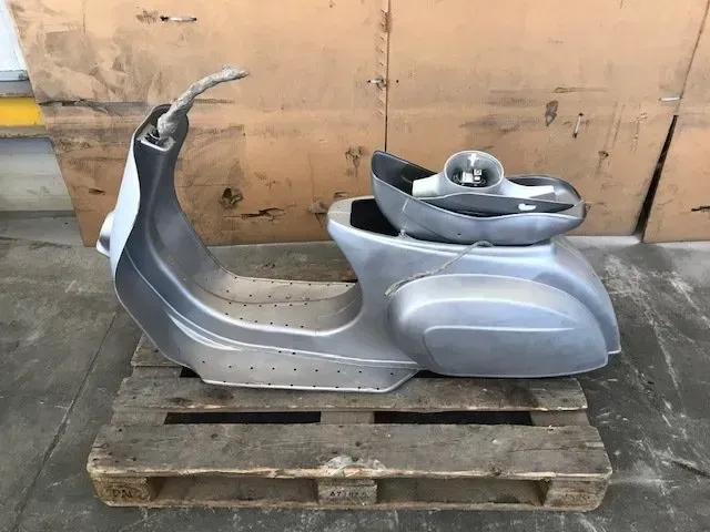 Carrozzeria di scooter argentata su un pallet di legno, appoggiata alla parete di un magazzino.