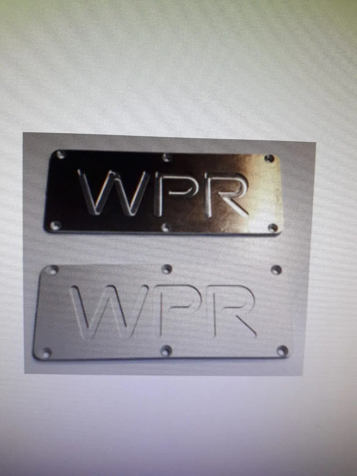Targhe metalliche con incisa la scritta “WPR”, una scura e una argentata, montate a parete.