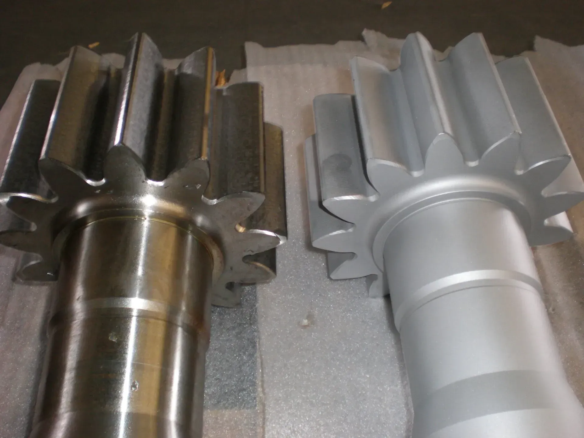 Due ingranaggi metallici, uno marrone scuro e uno argentato, giacciono uno accanto all'altro su una superficie.