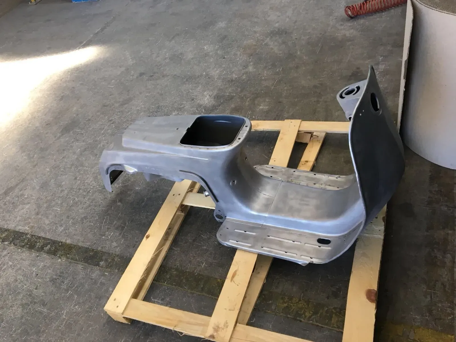 Un pannello grigio della carrozzeria di un'auto appoggiato su un pallet di legno in un garage o in un'officina.