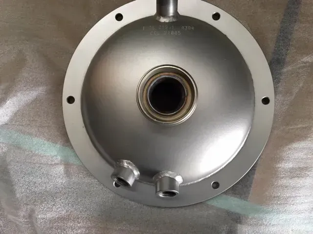 Componente metallico circolare color argento con un'apertura centrale e due piccoli raccordi nella parte inferiore.