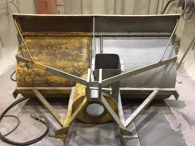 Vecchio accessorio spazzaneve in metallo con lama arrugginita e telaio triangolare bianco in un garage
