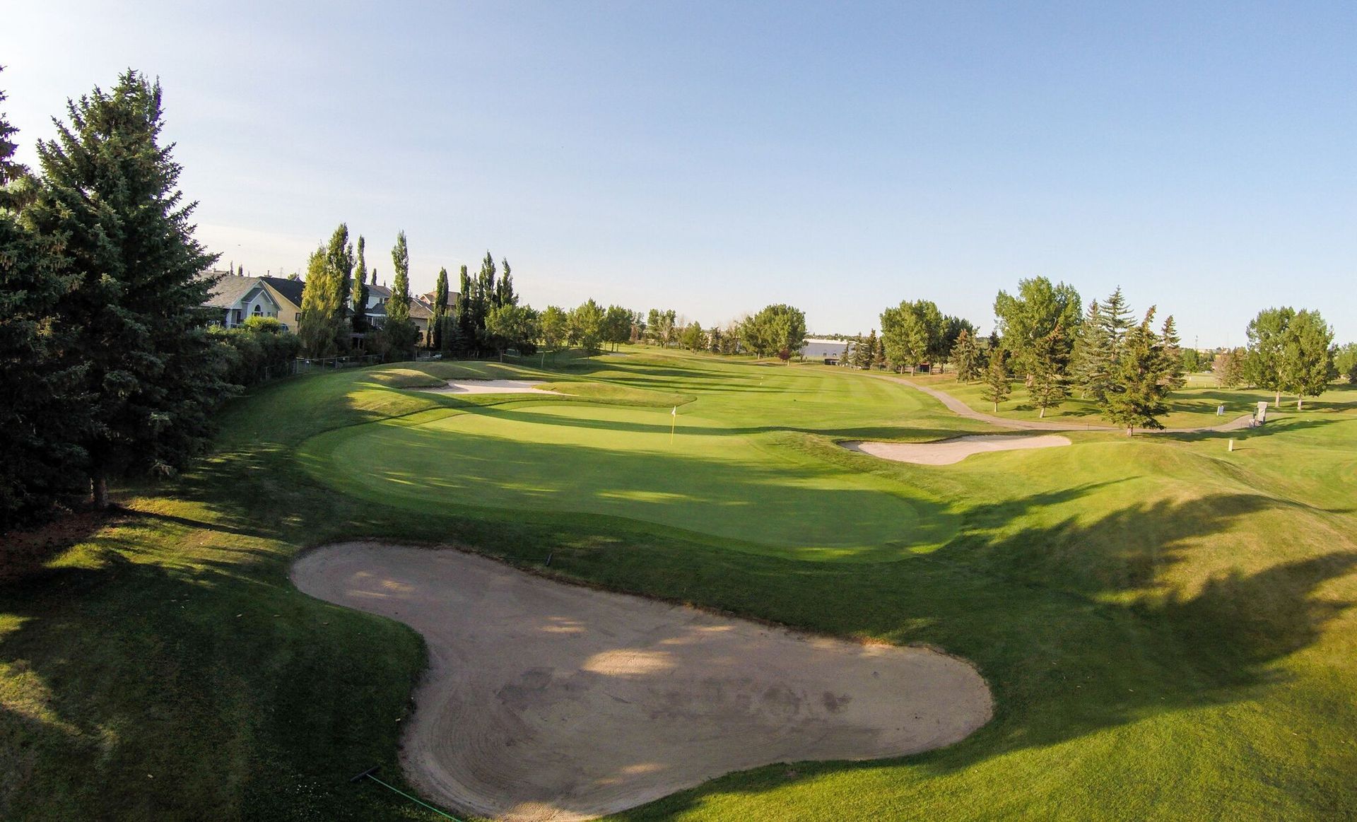 Golf course with green grass, sand traps, and trees under a clear, blue sky.