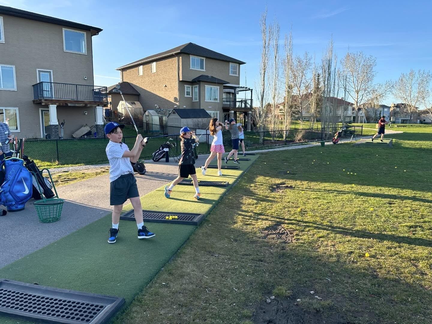 Kids practice golf swings on a driving range, sunny day.
