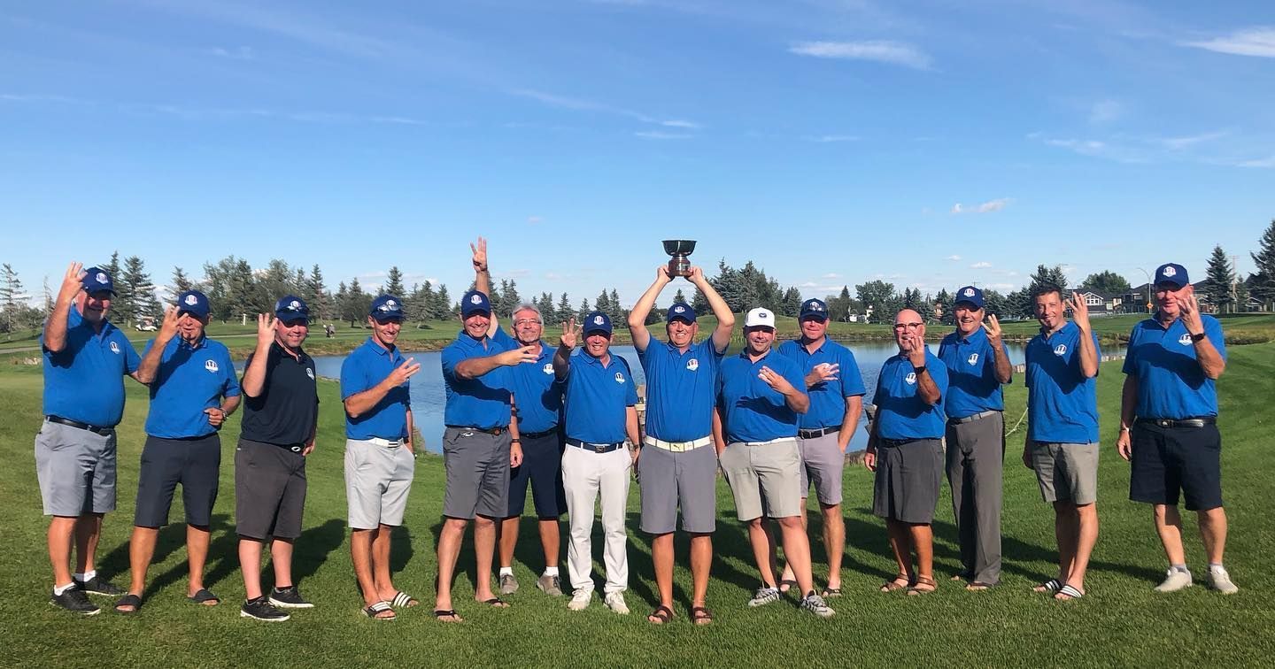 Group of men in blue shirts and hats holding a trophy on a golf course, cheering.