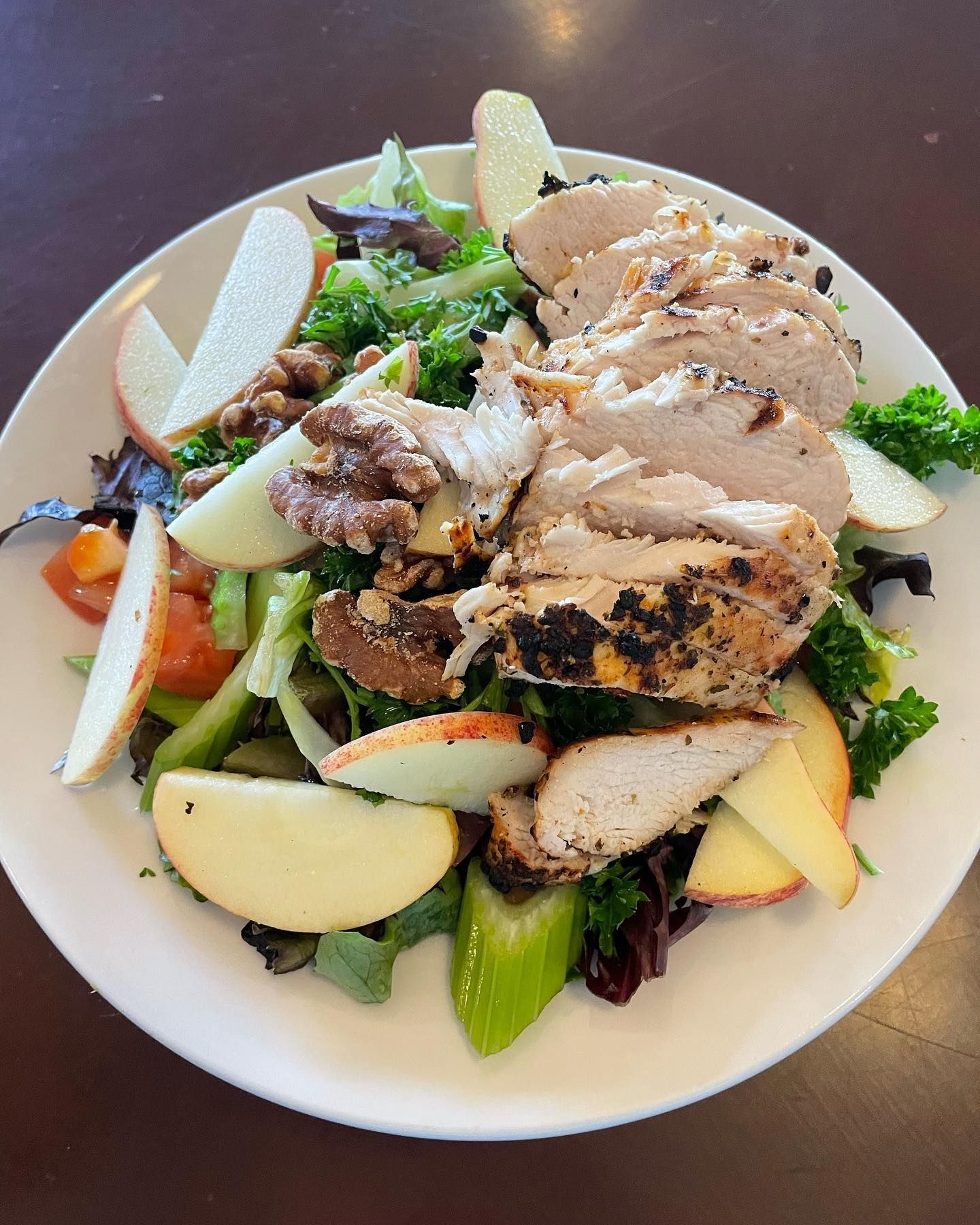 Salad with sliced chicken, apples, walnuts, greens on white plate.