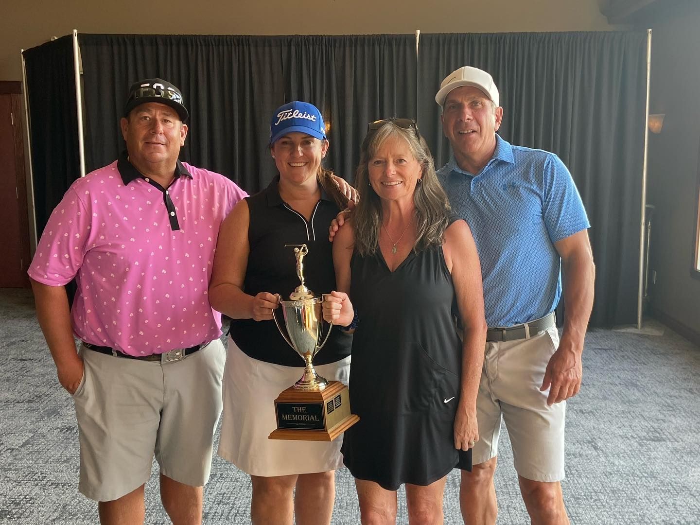 Four people pose with a trophy. Two men and two women smile indoors against a black backdrop.