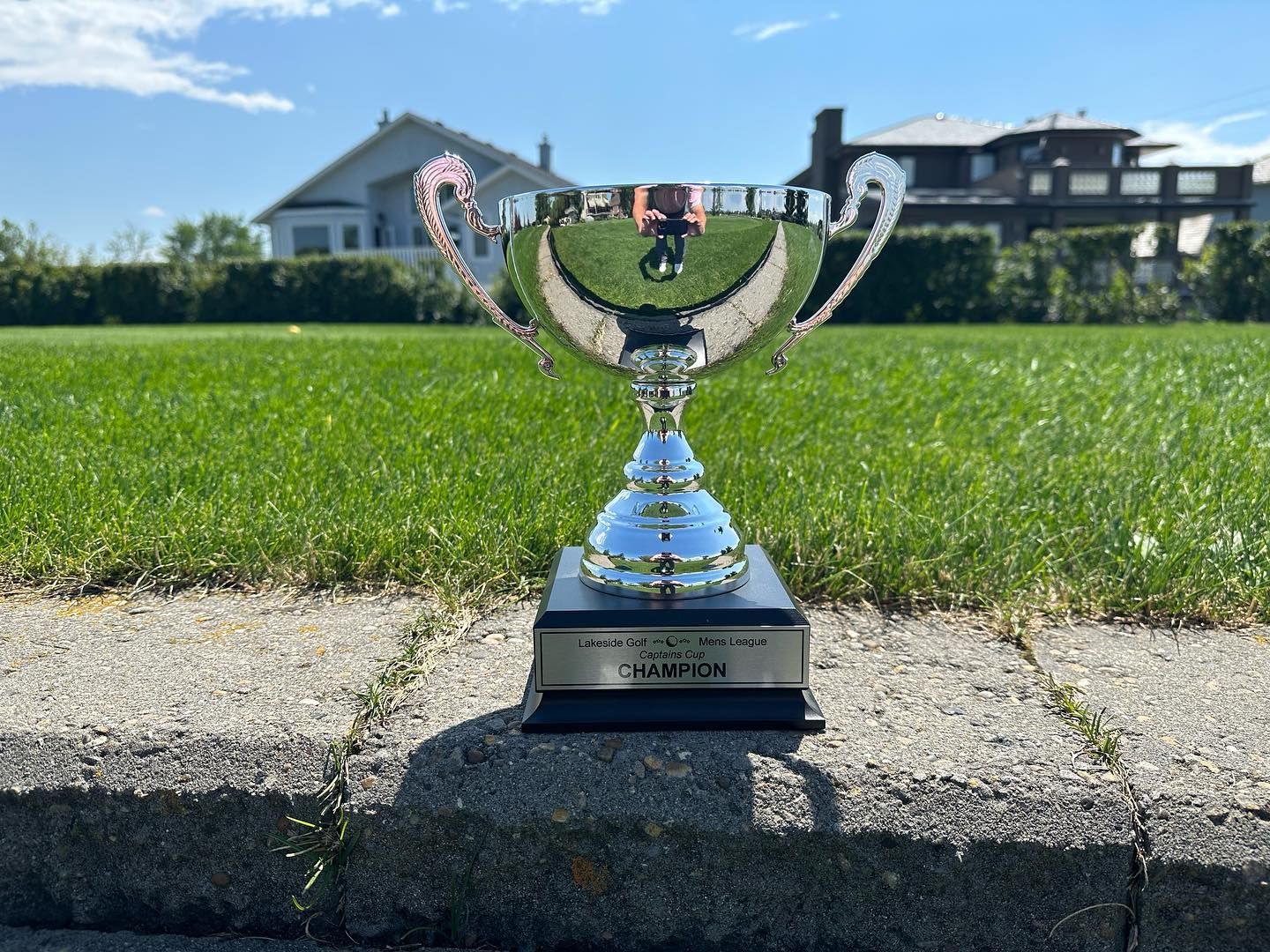 Silver trophy on a concrete ledge, grass and houses in the background on a sunny day.
