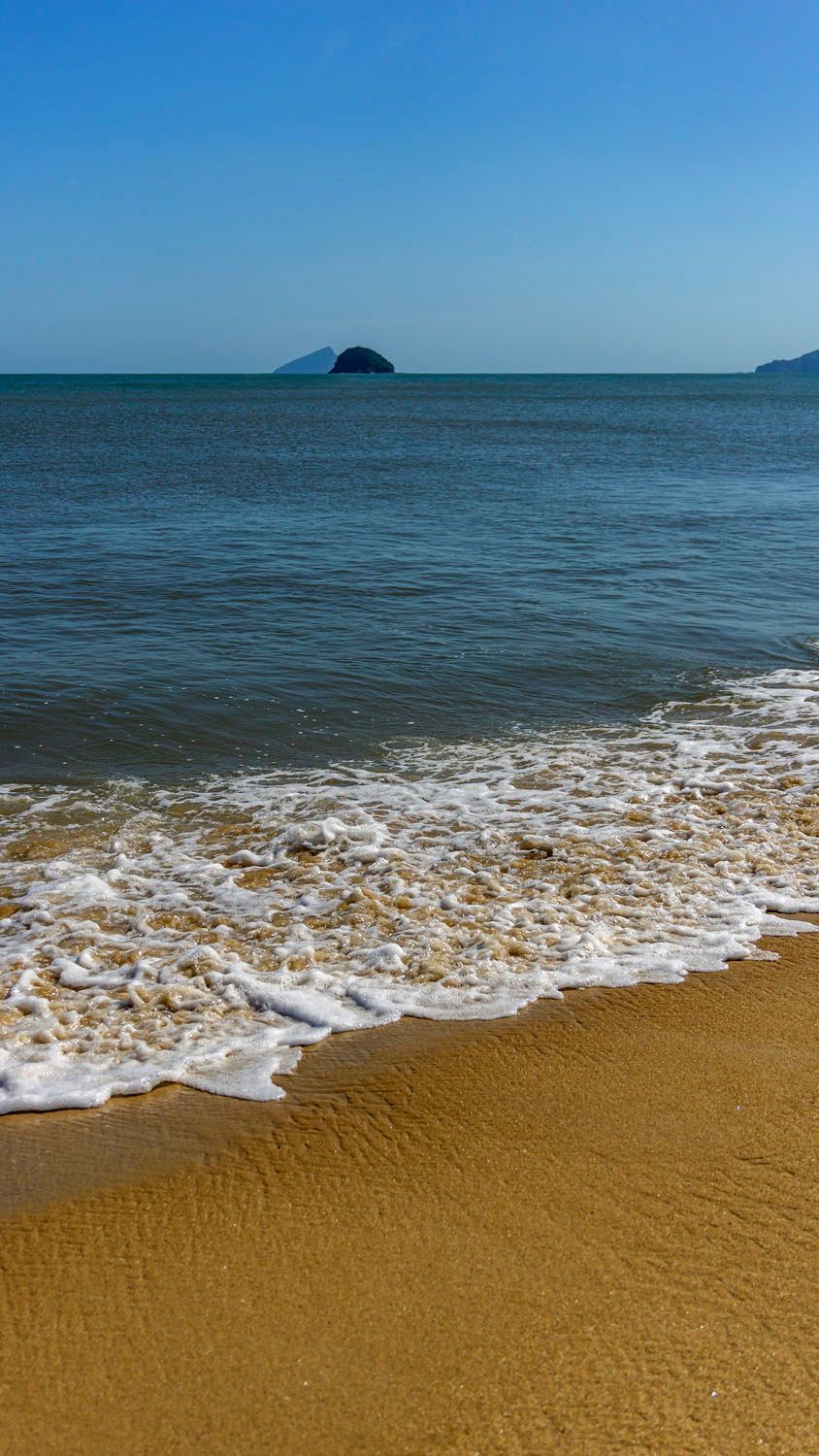 Uma praia com ondas quebrando na areia e um grande corpo de água ao fundo.