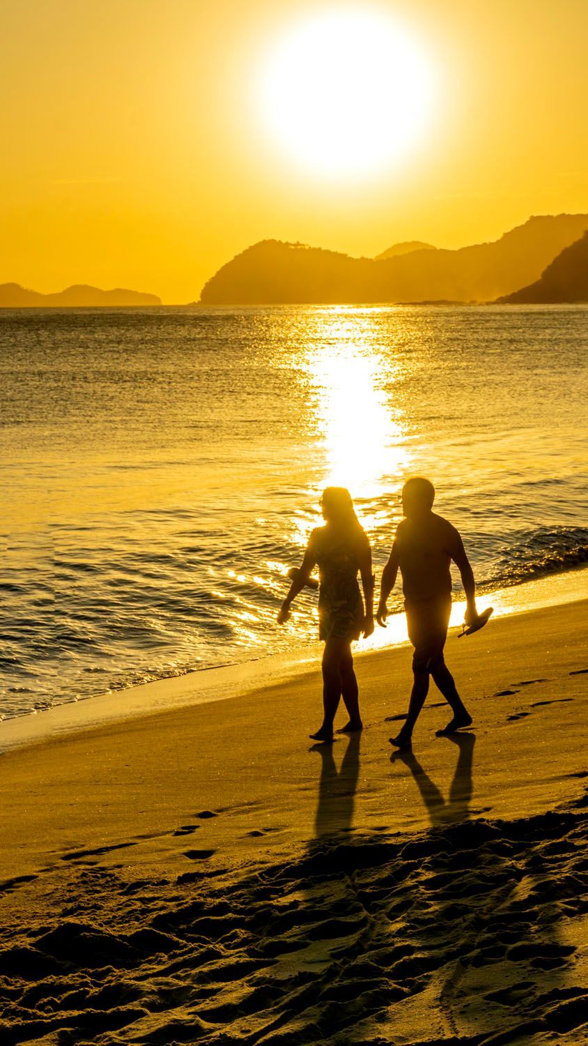 Um homem e uma mulher estão caminhando na praia ao pôr do sol.