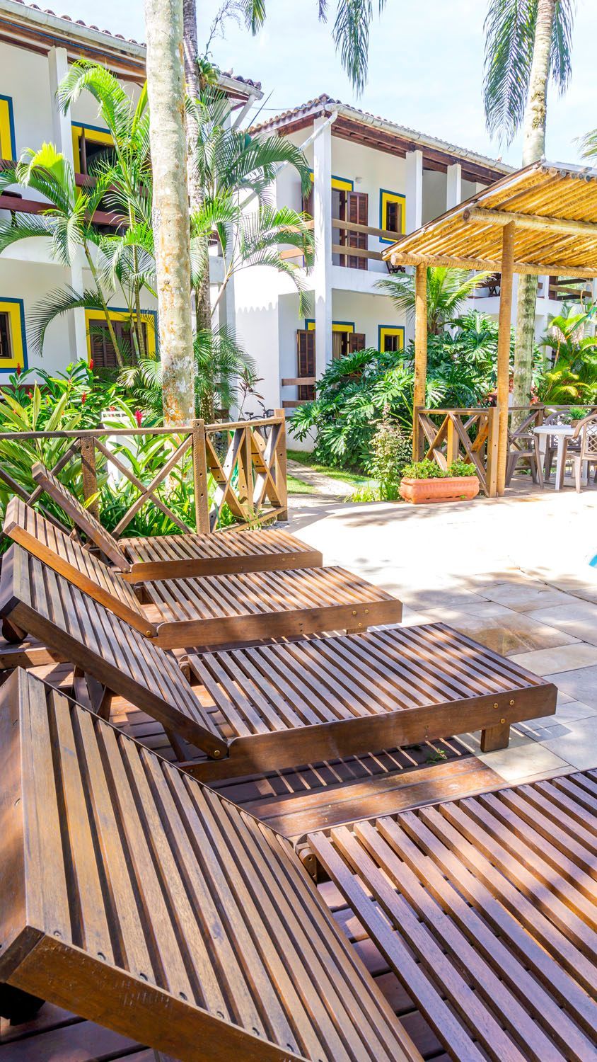 Uma fileira de espreguiçadeiras de madeira estão alinhadas ao lado de uma piscina.