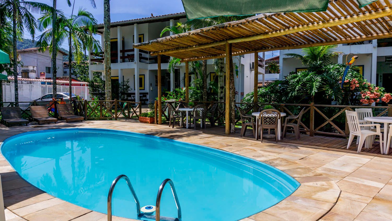 Há uma grande piscina em frente a uma casa cercada por palmeiras.