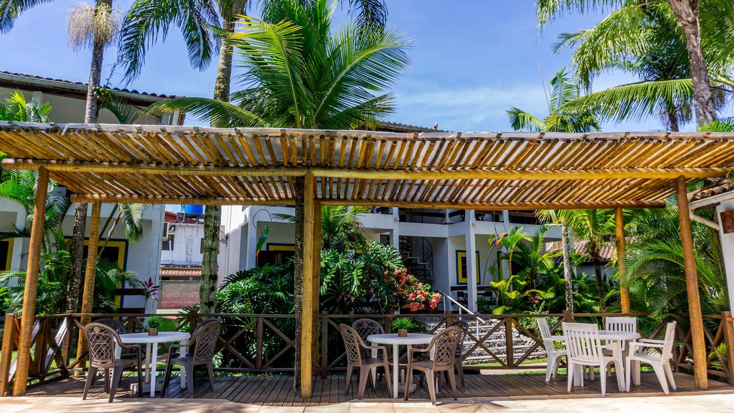 Uma pérgola de madeira com mesas e cadeiras embaixo dela.