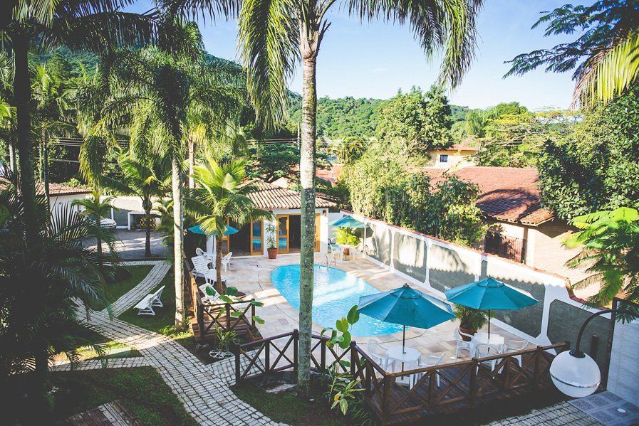 Vista aérea de uma piscina cercada por palmeiras e guarda-sóis