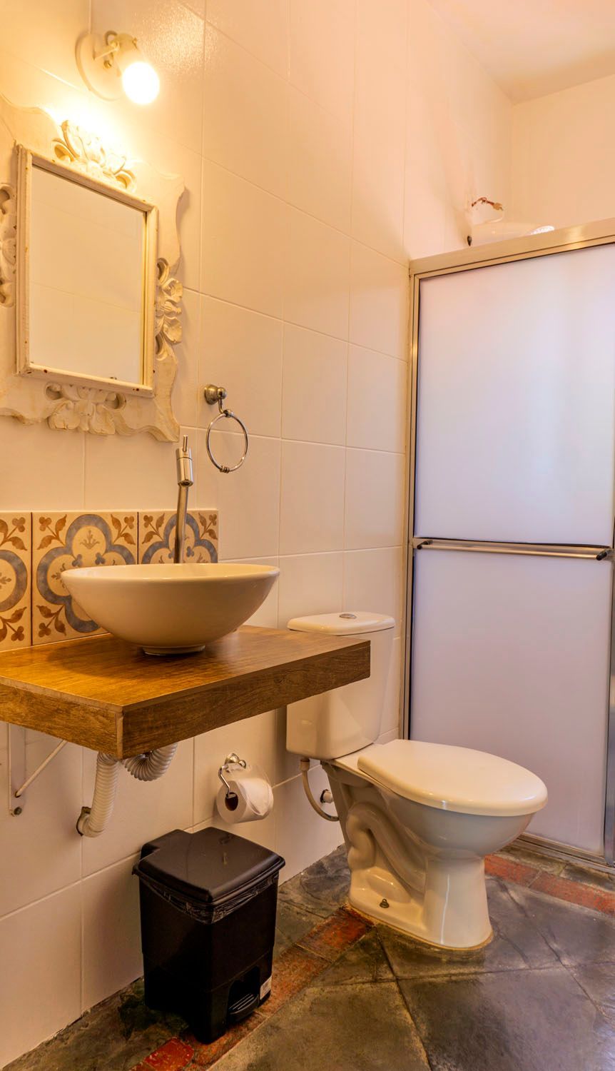 Um banheiro com pia, vaso sanitário, espelho e lata de lixo.