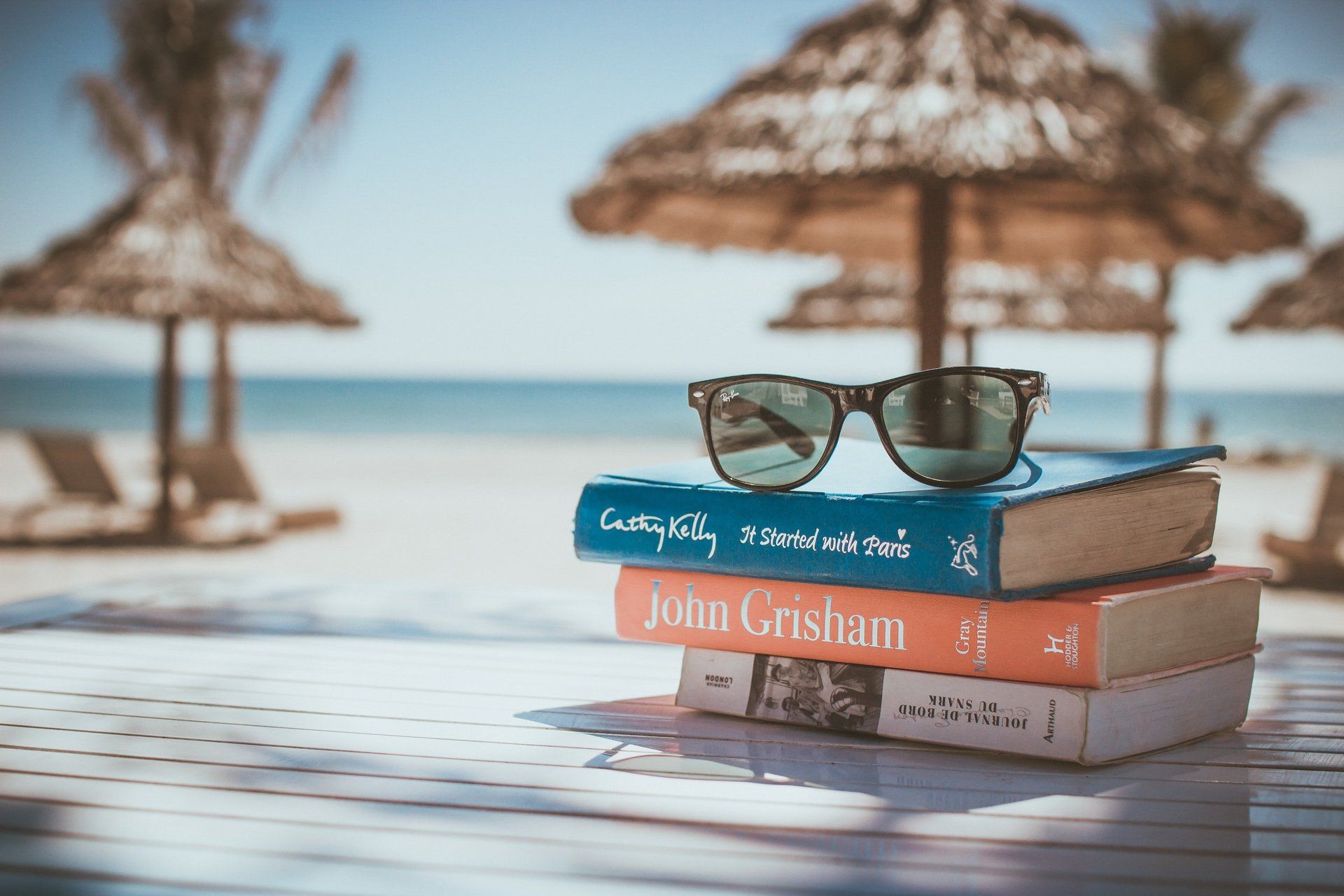 Uma pilha de livros com óculos de sol em cima deles em uma praia.