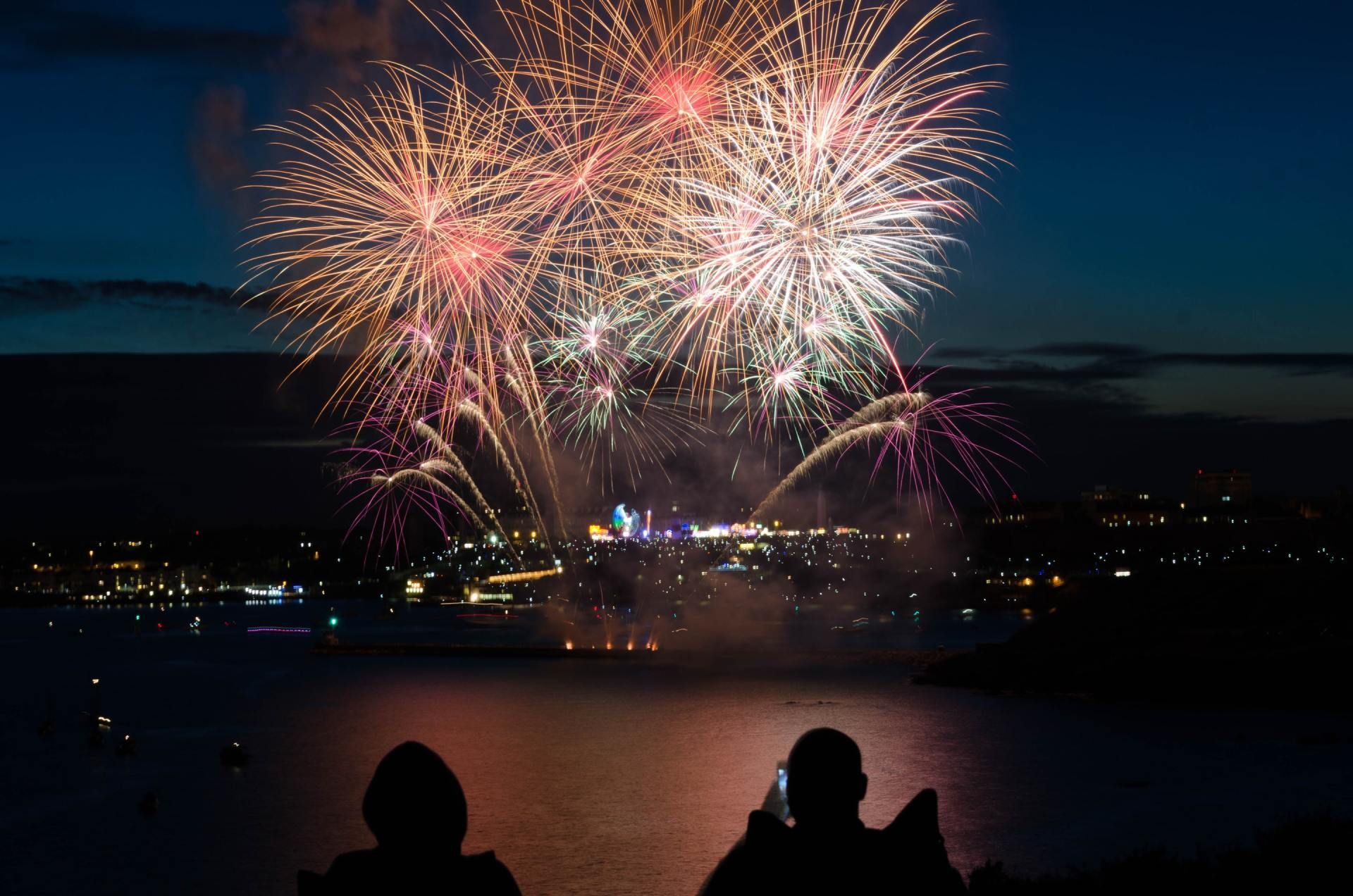 Duas pessoas estão assistindo a fogos de artifício sobre um corpo d'água.