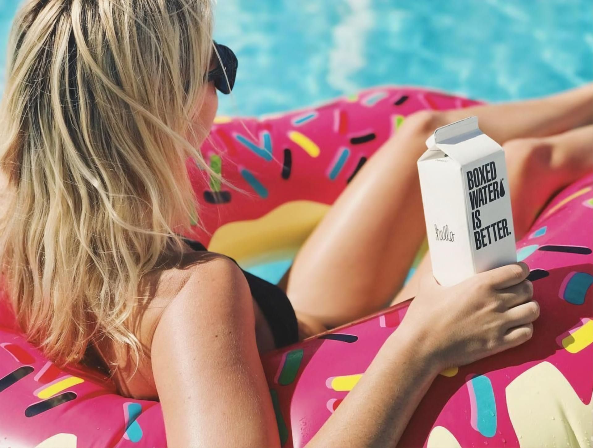 Uma mulher está flutuando em uma piscina segurando uma caixa de leite