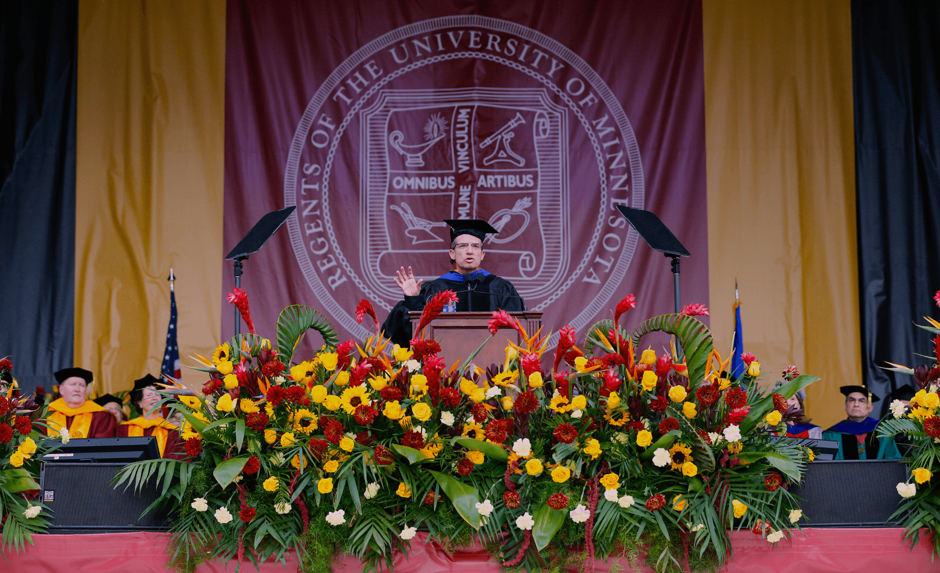 A man in a graduation cap and gown is giving a speech at the university of minnesota.