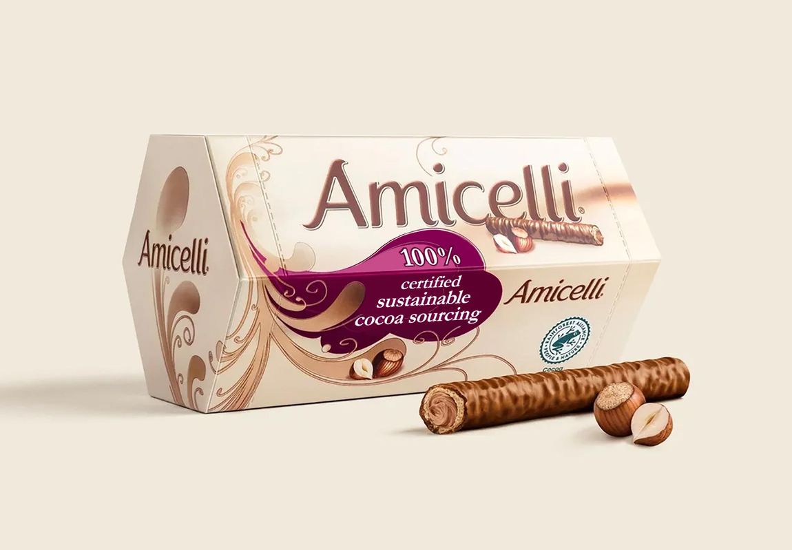 Produktabbildung der Amicelli 150 g Verpackung. Davor liegt ein Waffelröllchen und zwei Haselnüsse.