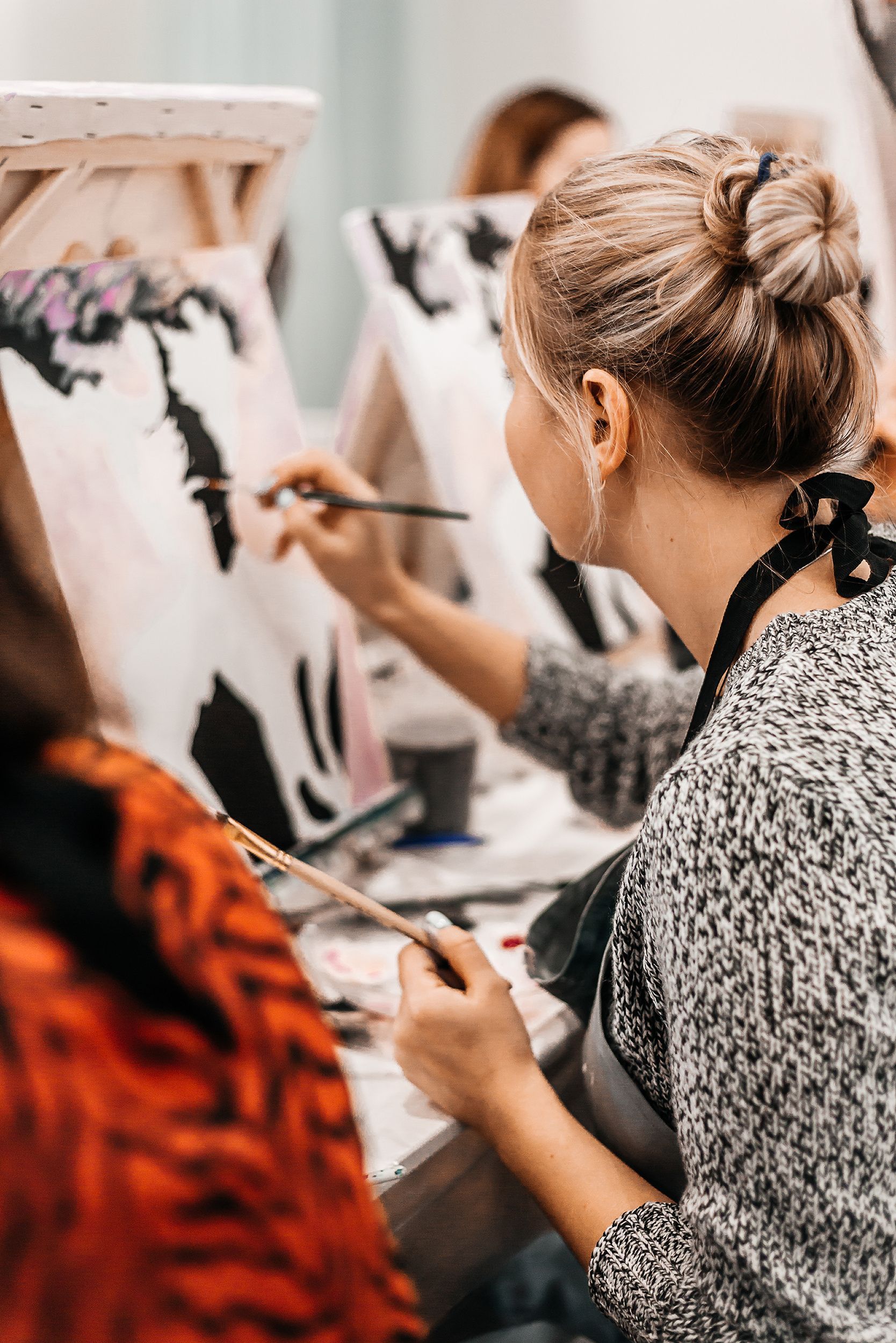 A woman is sitting at a table painting on an easel.