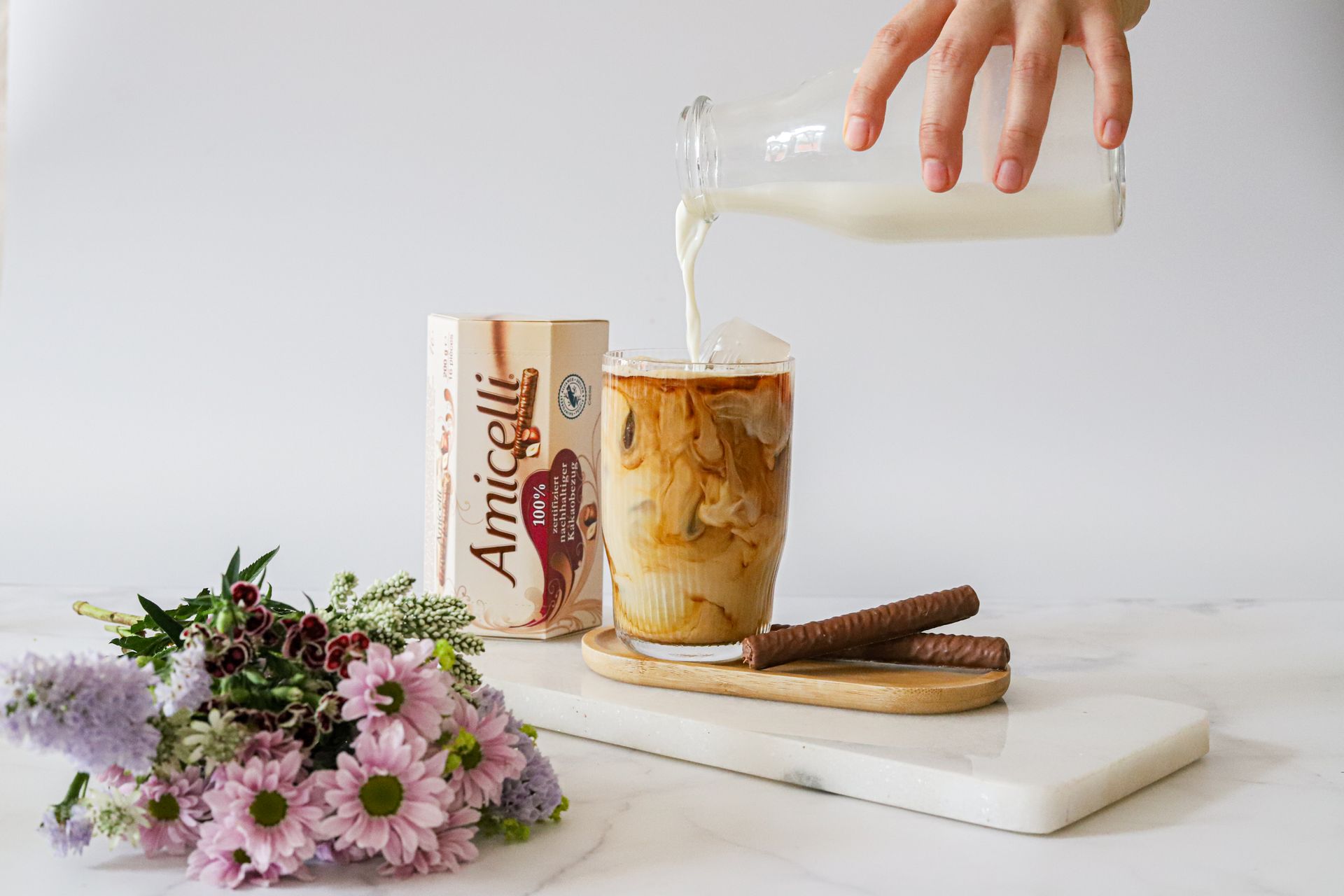 A person is pouring milk into a cup of iced coffee with amicelli.