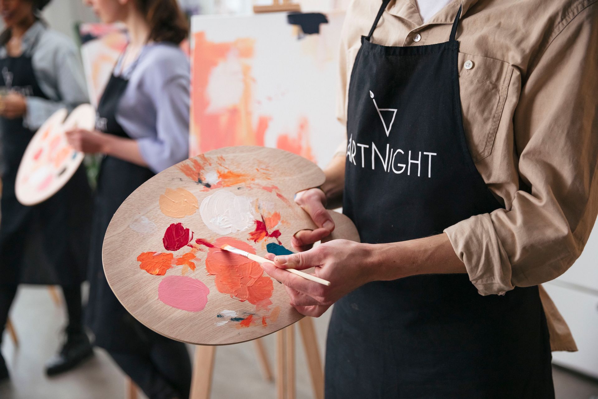 A person in an apron is holding a palette of paint and a brush.