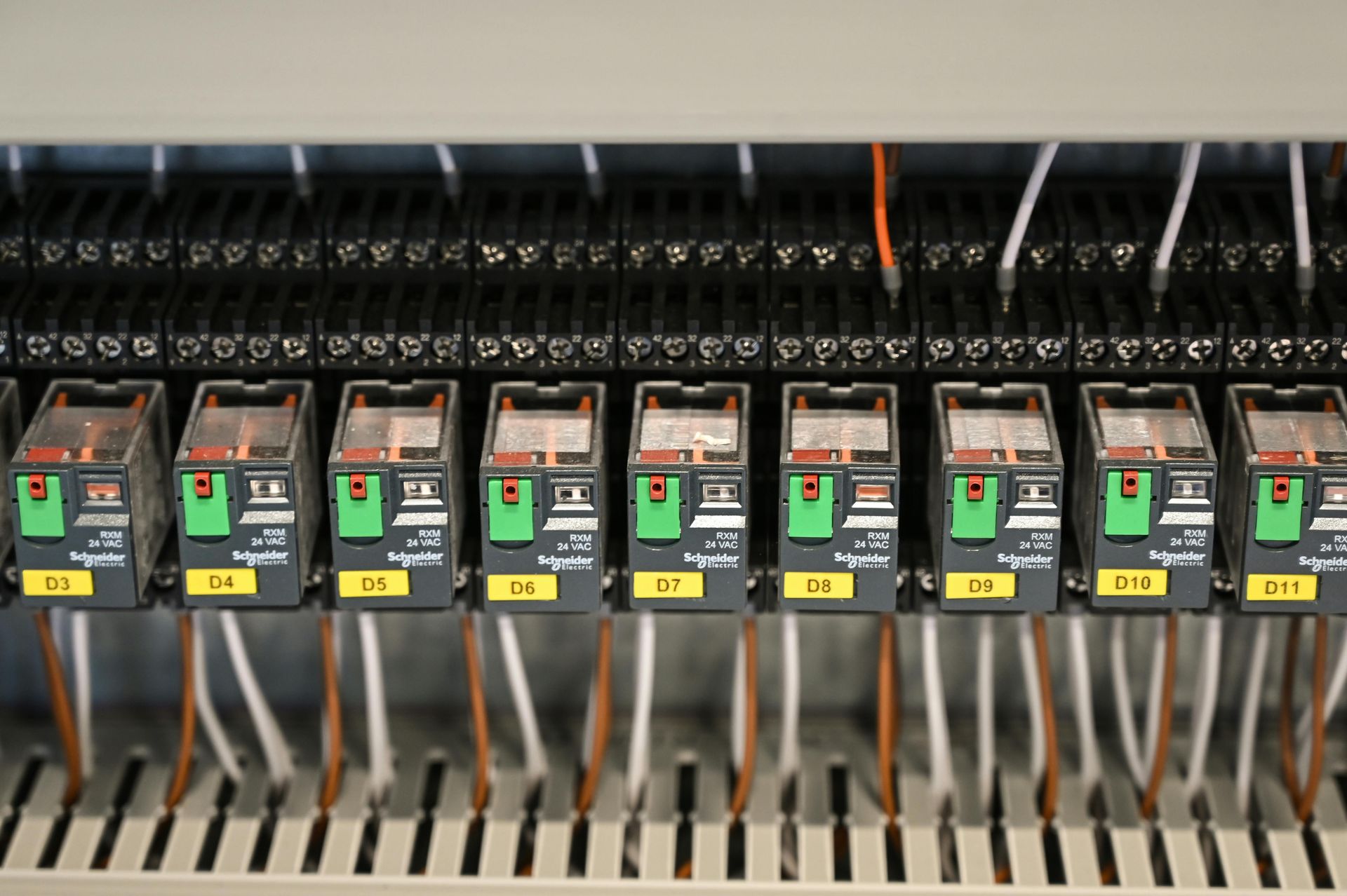 A row of Schneider Electric industrial relays mounted on a terminal block rail inside an electrical control cabinet.