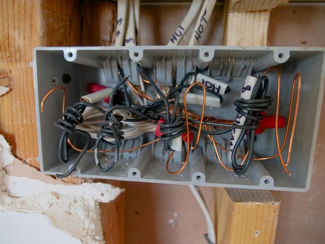 An open grey electrical junction box mounted on a wooden wall stud, containing several connected and looped wires.