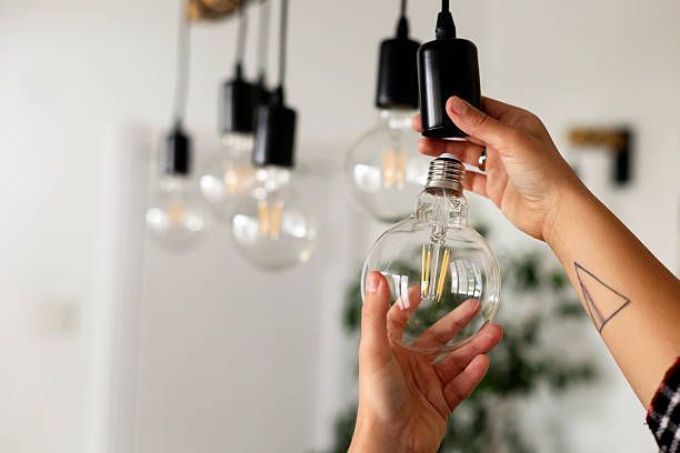 A person installing a large, globe-shaped Edison light bulb into a pendant lamp fixture.