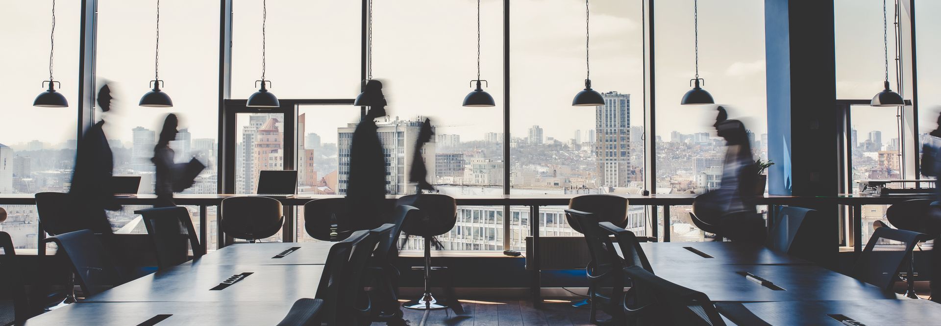 A group of people are sitting at desks in an office with a view of the city.