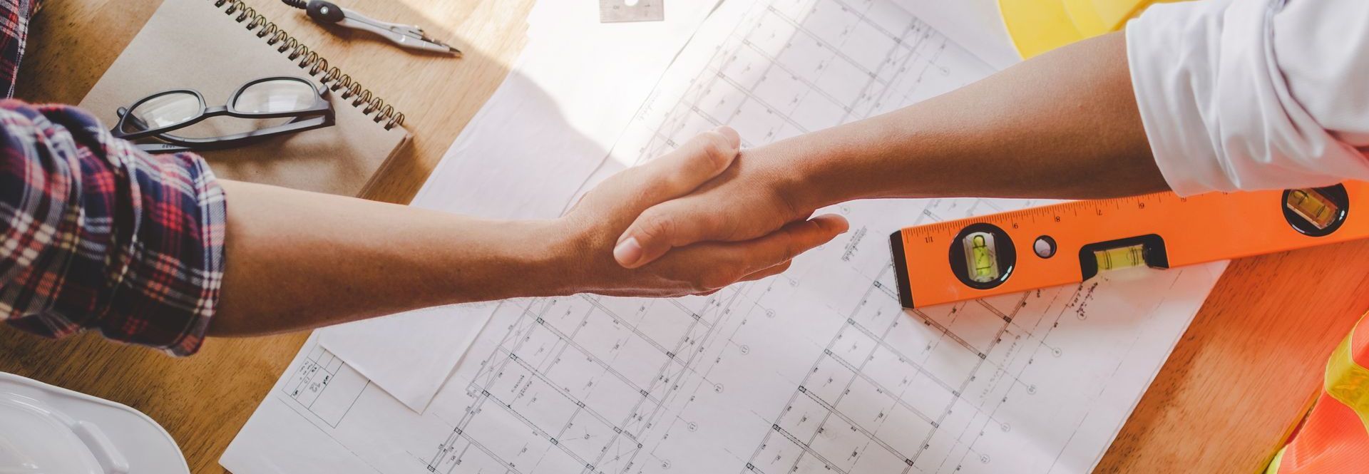 Two men are shaking hands over a table with blueprints.