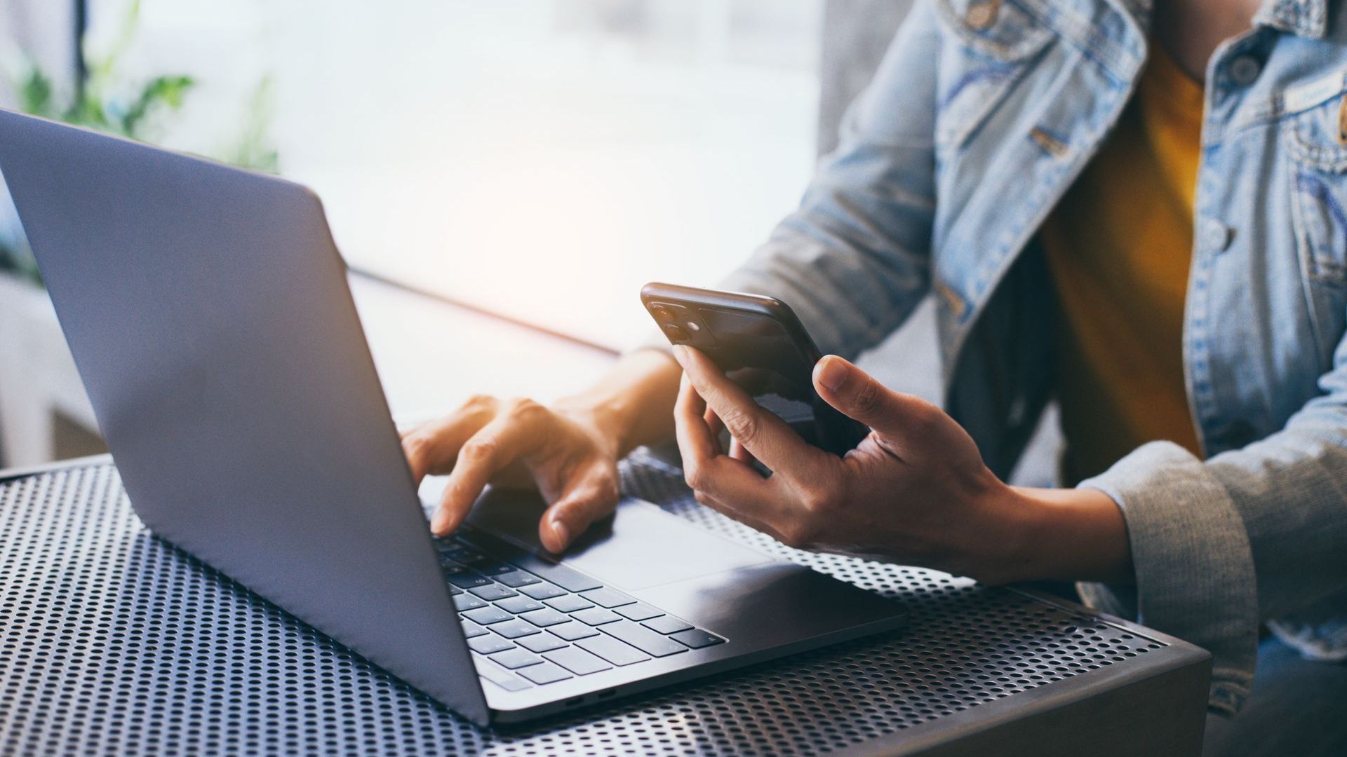 A woman is using a laptop and a cell phone at the same time.