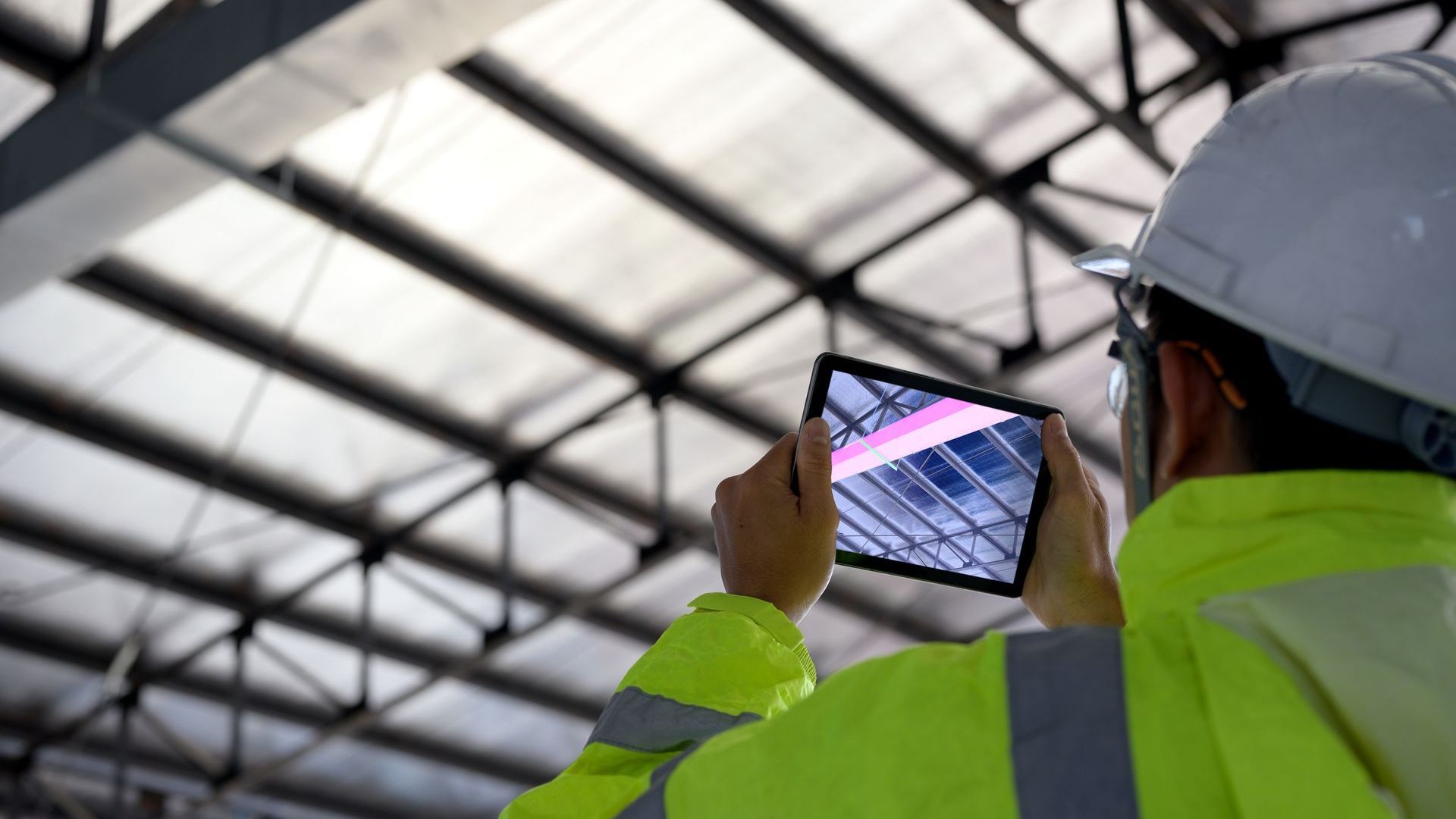 A construction worker is taking a picture of a roof with a tablet.