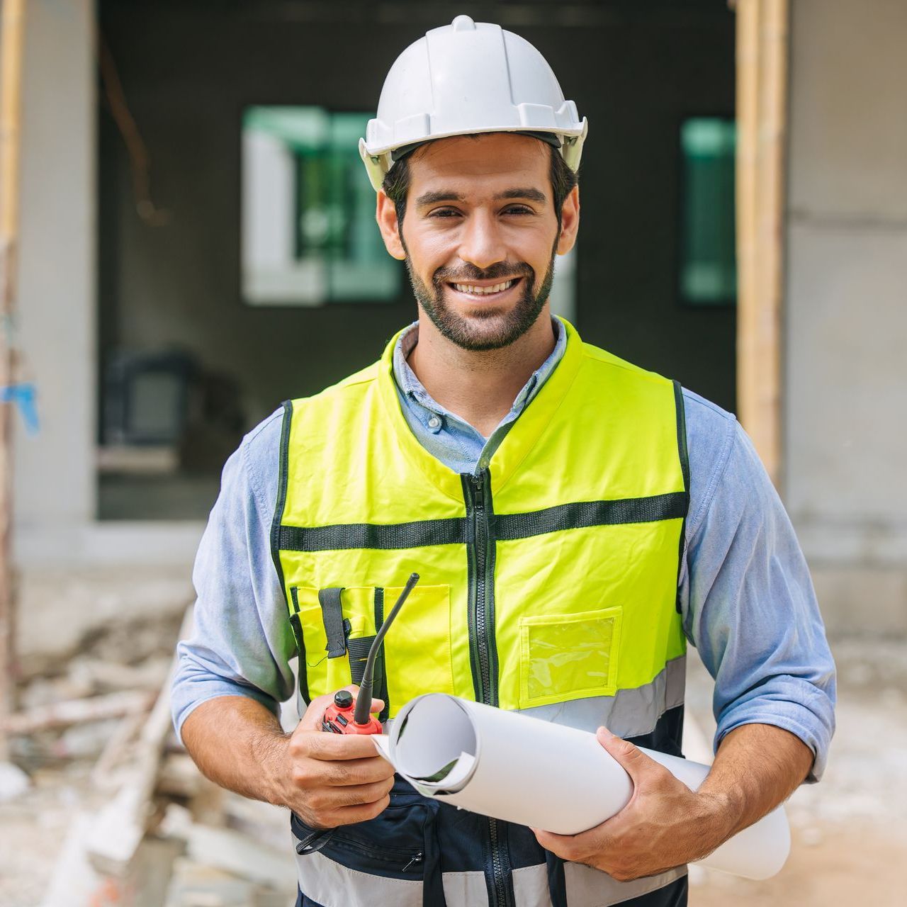 A construction worker wearing a hard hat and safety vest is holding a blueprint.
