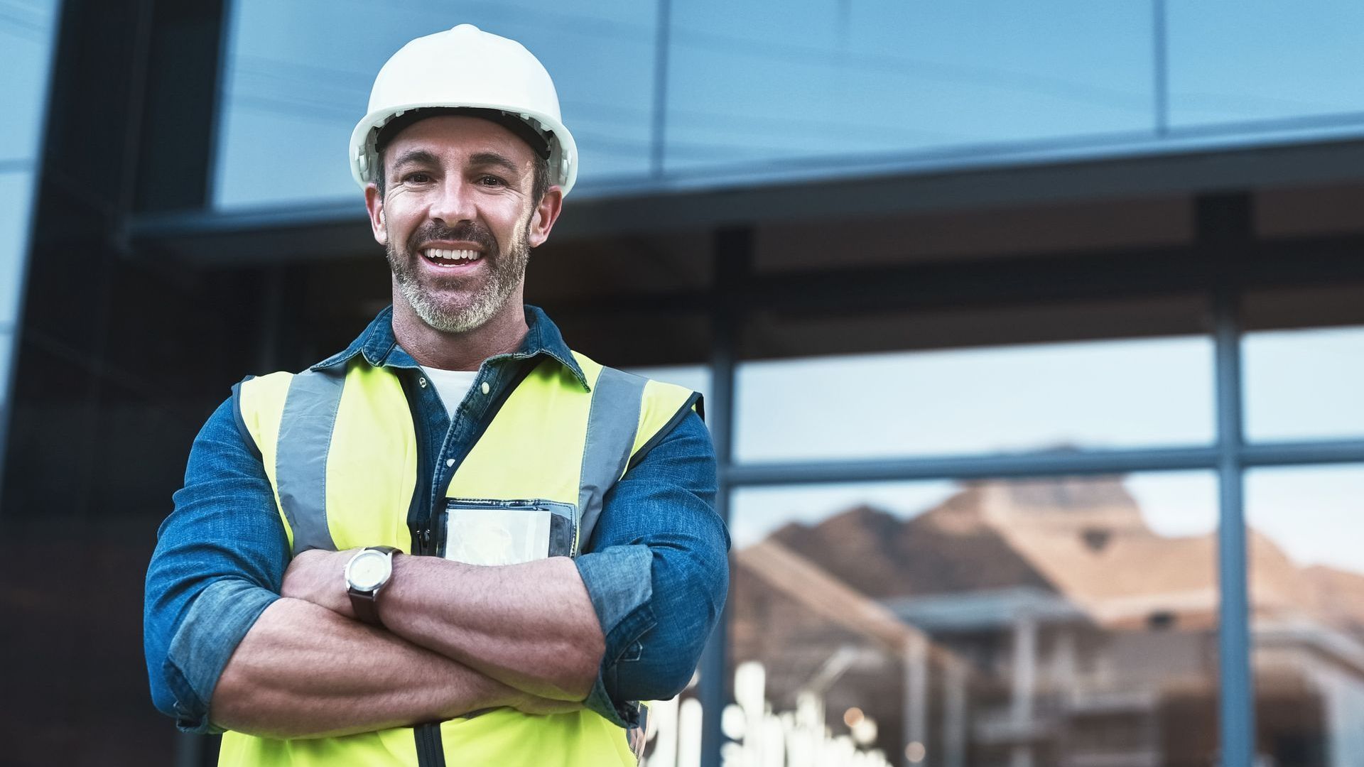 A man wearing a hard hat and safety vest is standing with his arms crossed.
