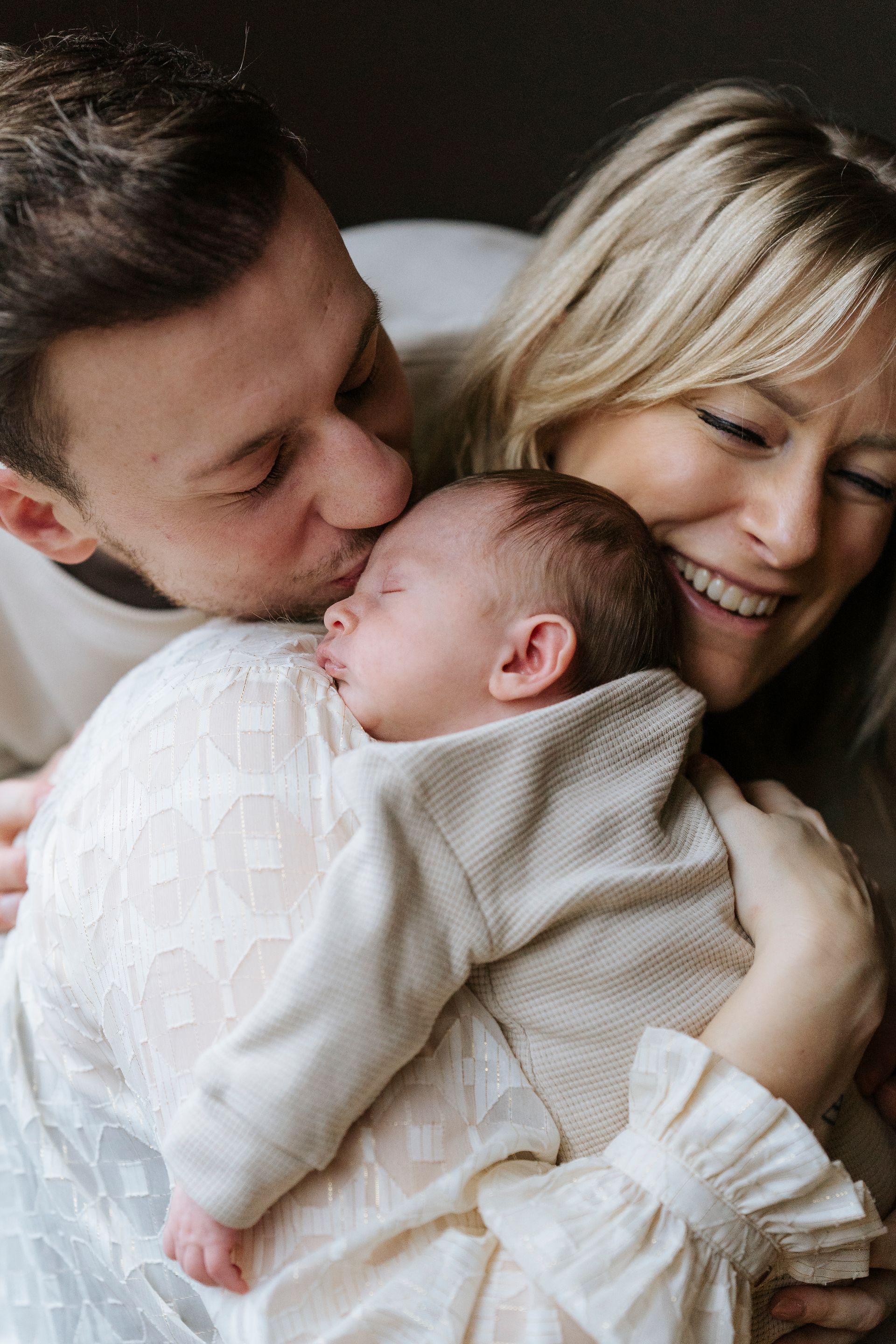 Ouders kussen pasgeboren baby; moeder houdt baby vast.