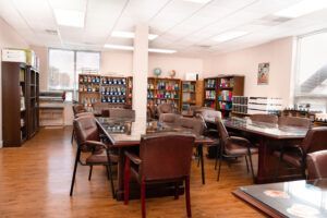 A room with tables and chairs, books on shelves, and windows.
