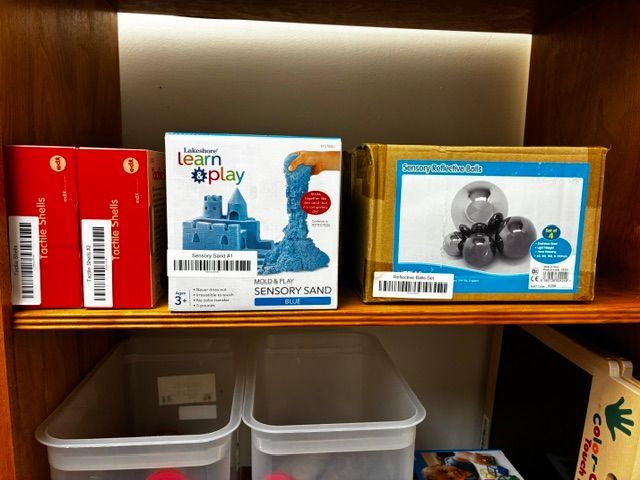 Wooden shelf with boxed toys and two clear storage bins underneath
