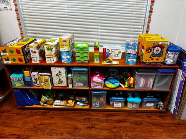 Toy-filled shelving unit in a room with colorful boxes and bins under a window with blinds