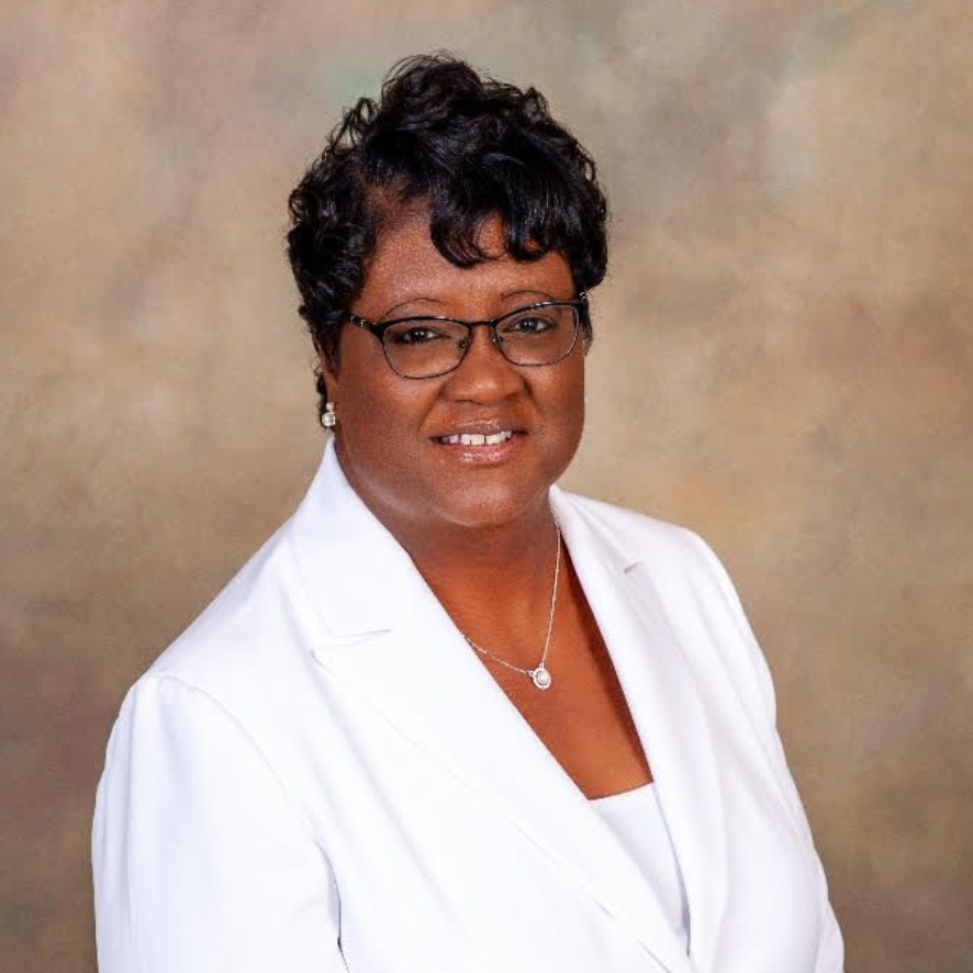 A woman in a white blazer and glasses smiles at the camera.