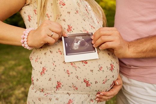pregnant lady in flower dress holding ultrasound image over belly