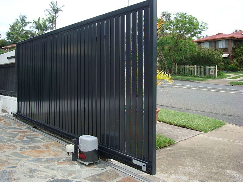 A dark gray sliding driveway gate, partially open, with an automatic opener.